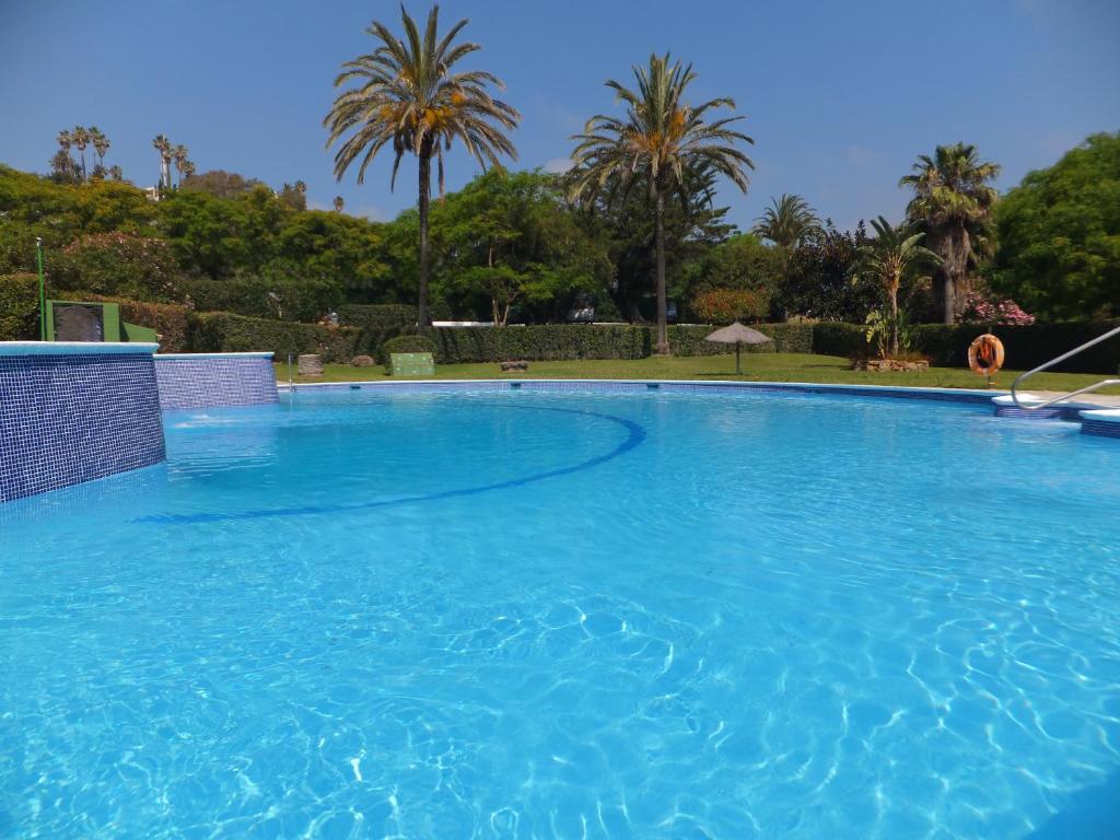 una gran piscina azul con palmeras en el fondo en Apartamento Bahia Dorada, en Estepona