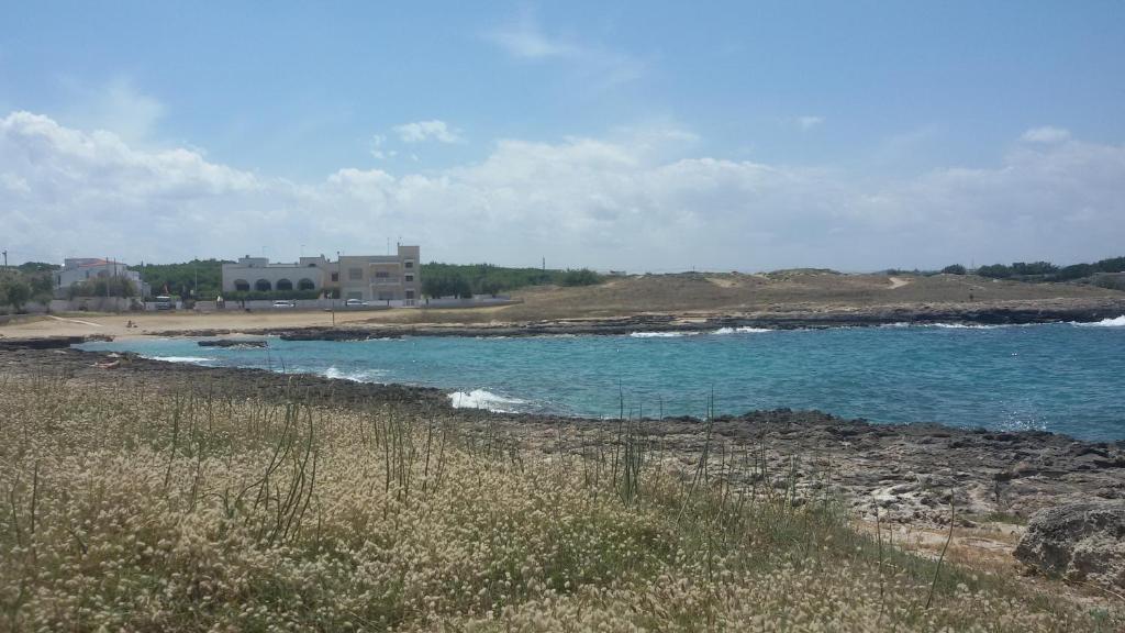 a beach with blue water and a house in the background at Hotel Corallo in Torre Santa Sabina