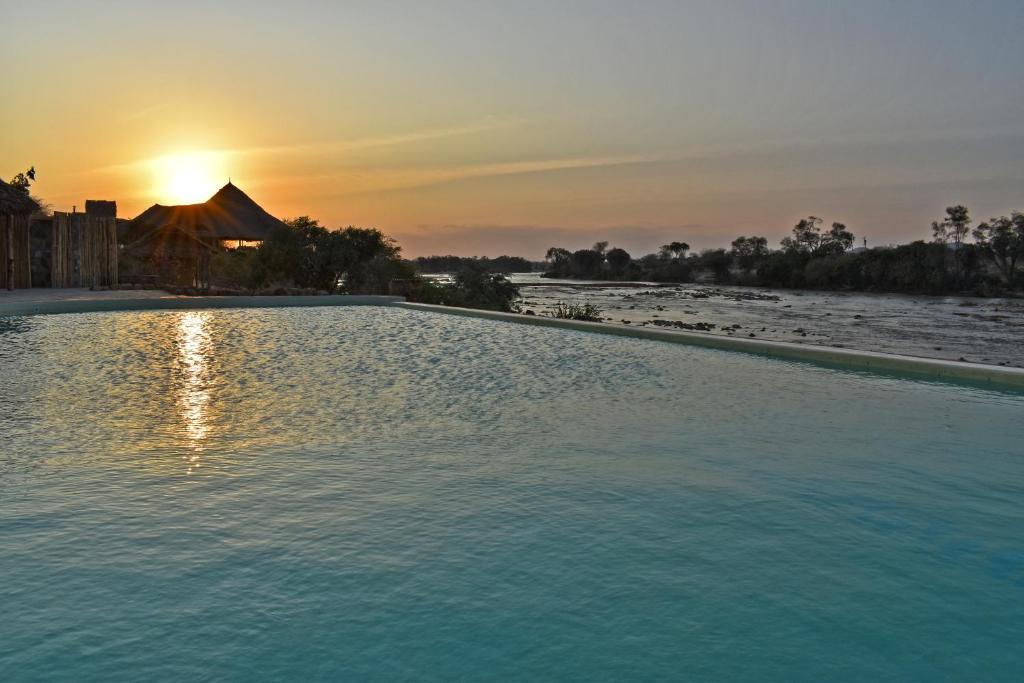 una piscina con puesta de sol en el fondo en Kiboko River Camp, en Koito