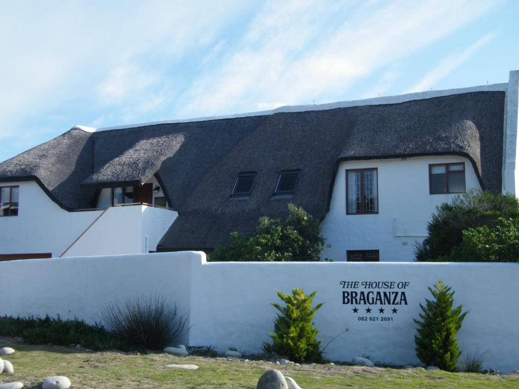 a house with a thatched roof behind a white fence at The House of Braganza in Kommetjie