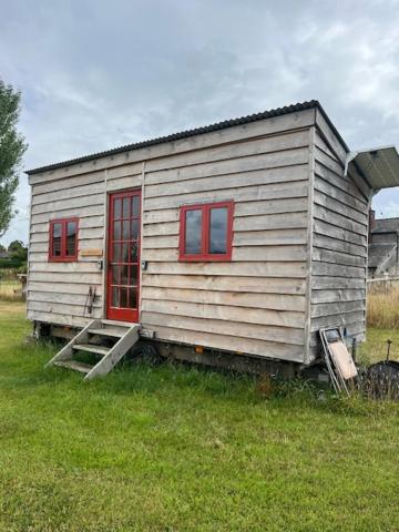 a small house with red windows in a field at Black Bridge Cabin in Lyonshall