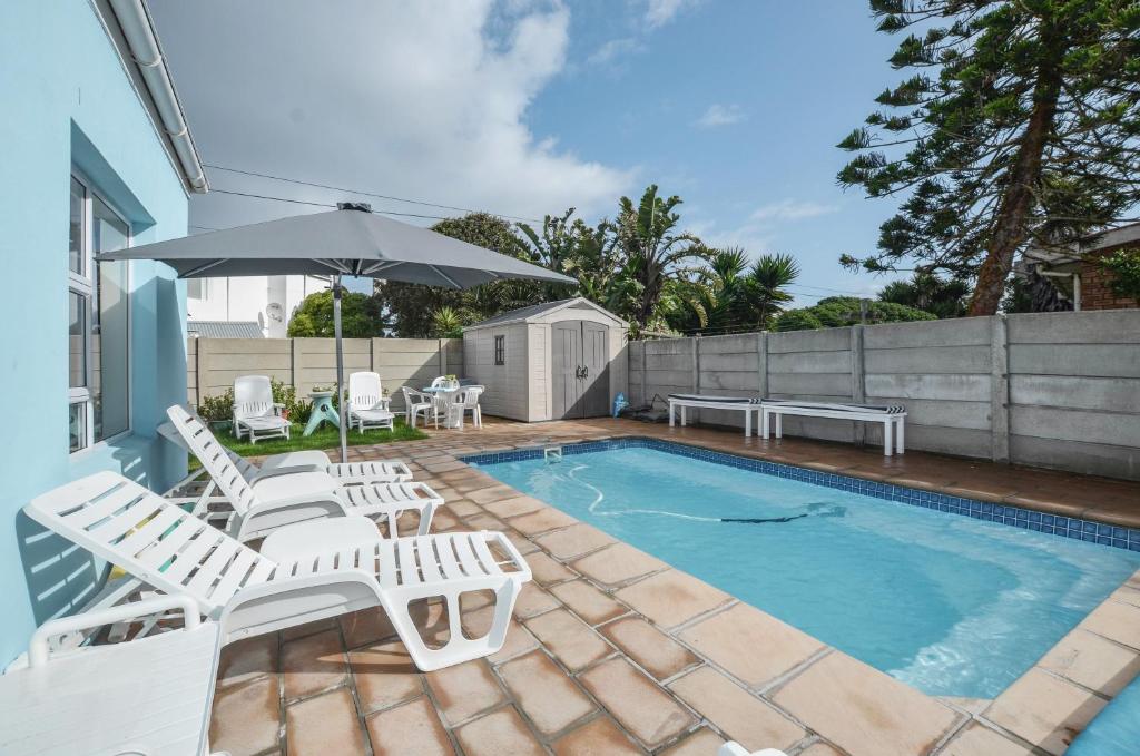 a swimming pool with white chairs and an umbrella at Family Tides in Yzerfontein