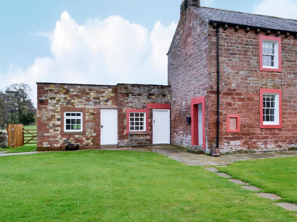 an old brick building with red doors and a yard at The Cottage At 1710 in Castle Carrock