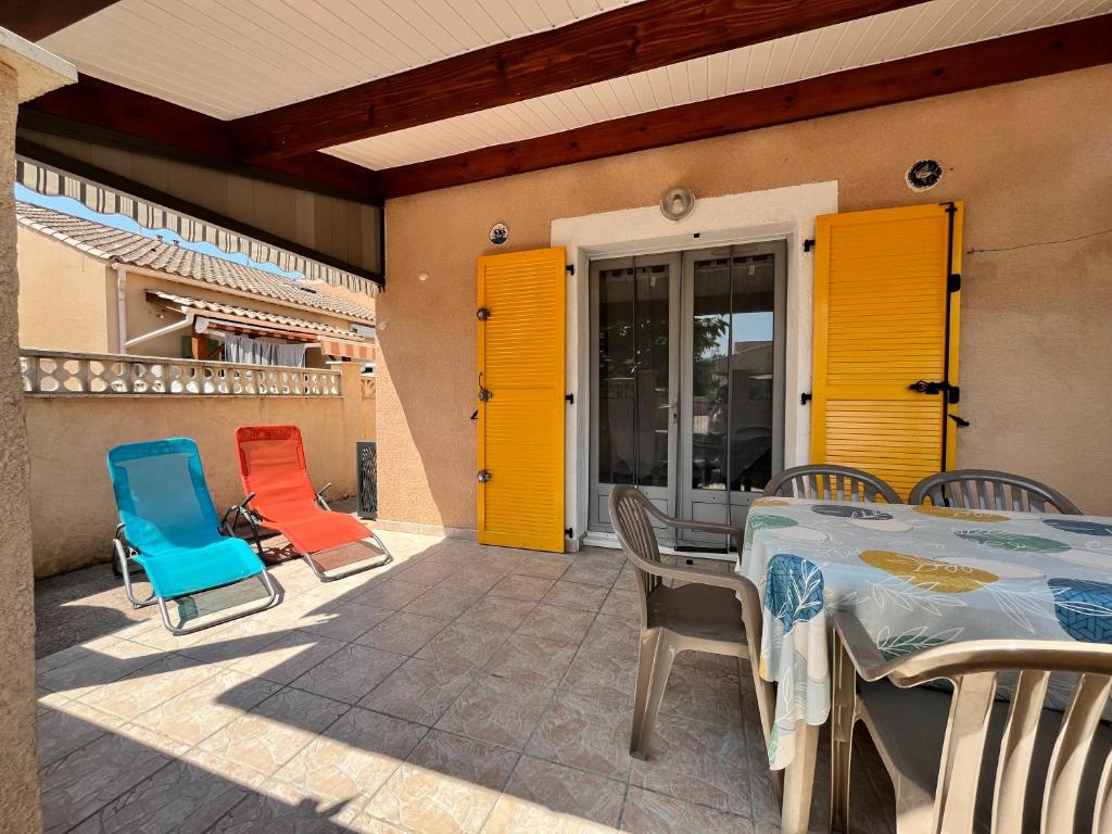 un patio avec des portes jaunes et une table et des chaises dans l'établissement Belle villa d'angle, 6 couchages, cuisine climatisée, 3 chambres terrasse ombragée parking dans résidence sécurisée avec piscine commune, 400 m de la mer, LROND24, à Portiragnes