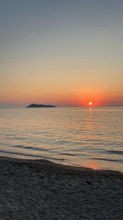 a sunset on the beach with an island in the water at Agapis Apartments in Petra