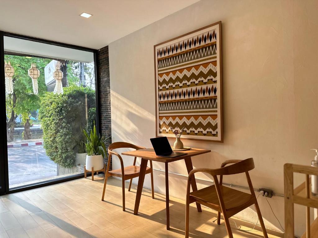 A sunlit shared workspace with a small table, two chairs and an open laptop beside a window.
