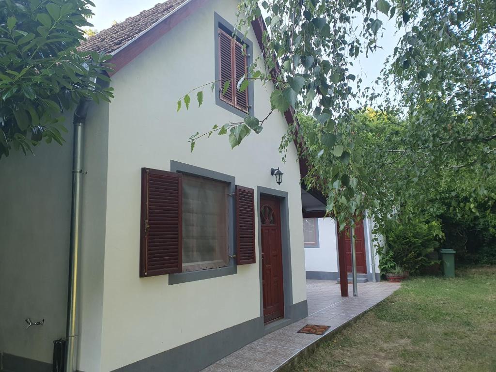 a white house with brown shuttered windows and a yard at Bacshegyi Vendeghaz 2 in Káptalantóti
