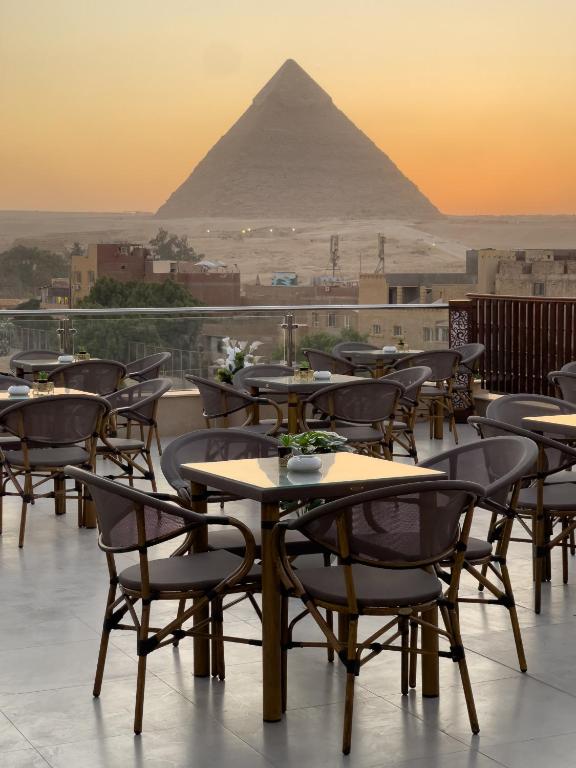 a group of tables and chairs with a pyramid in the background at AKHNATON Pyramids View Hotel With Rooftop Access & free airport pickup in Cairo