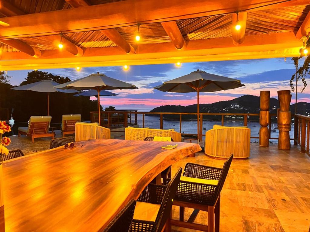 une grande table en bois avec des chaises et des parasols sur une terrasse dans l'établissement Zihuatanejo Luxury Villa - Events & Vacations, à Zihuatanejo