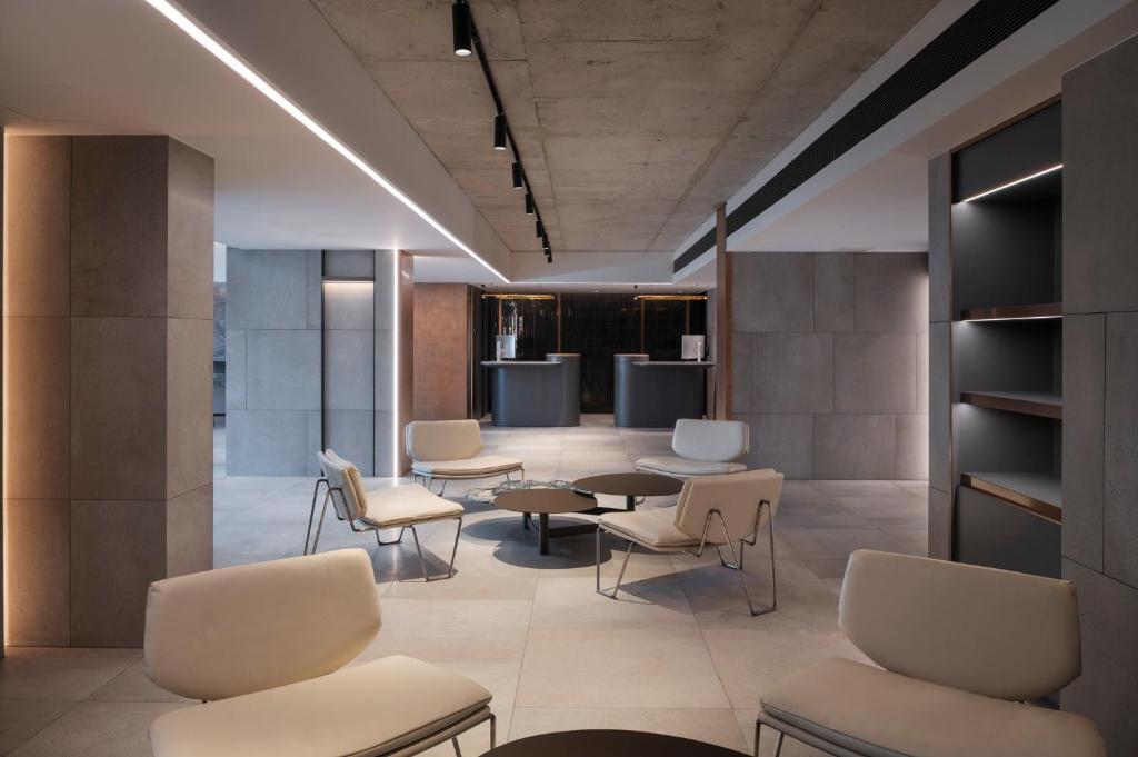 A quiet lounge area with light upholstered chairs, low tables and a dark service counter beyond.