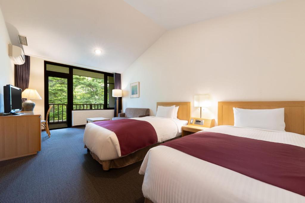 a hotel room with two beds and a television at Yatsugatake Kogen Lodge in Minamimaki