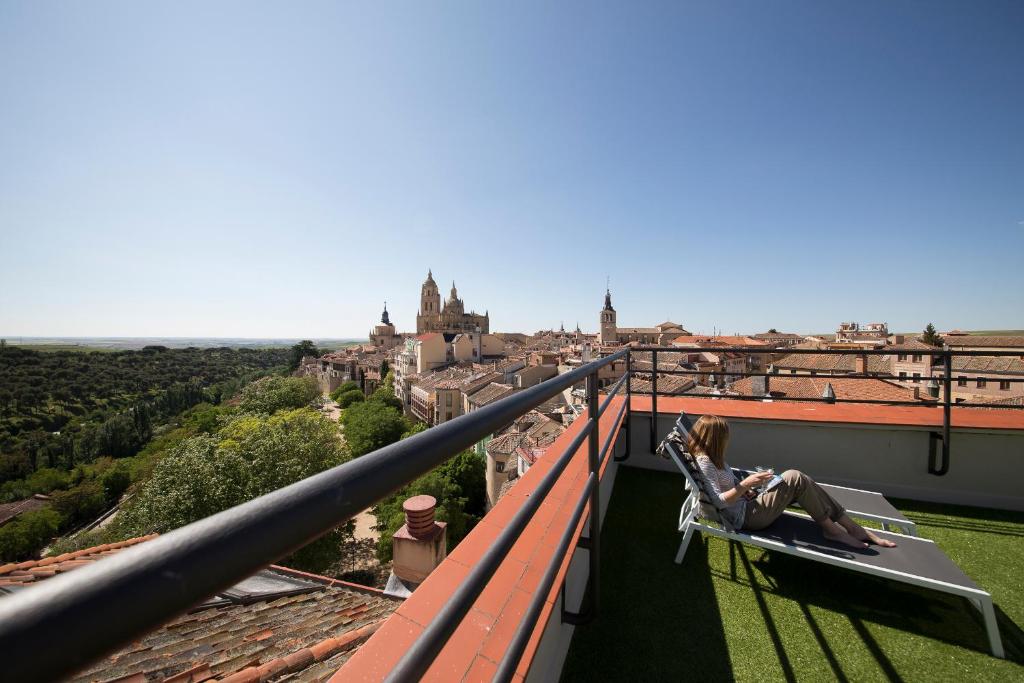 Eine Frau auf einem Stuhl auf einem Balkon mit Blick auf eine Stadt. in der Unterkunft Real Segovia by Recordis Hotels in Segovia