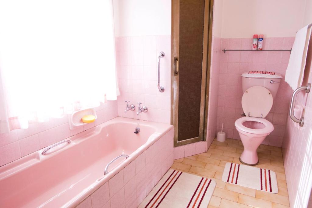 Baño de color rosa con bañera y aseo en Luisa's Place, en Pretoria