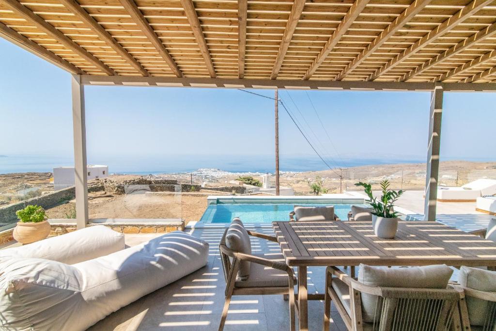 eine Terrasse mit Tisch und Stühlen und einem Pool in der Unterkunft Horizon Hill Villa in Tinos