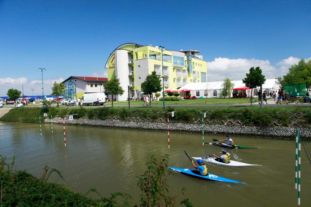 three people in kayaks on a river with a building at Hotel and Park Divoká Voda in Bratislava