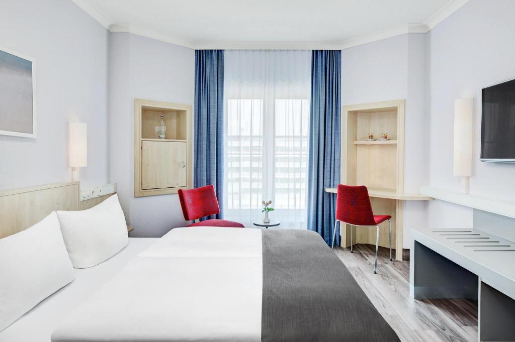 a hotel room with a bed and two red chairs at IntercityHotel Rostock in Rostock