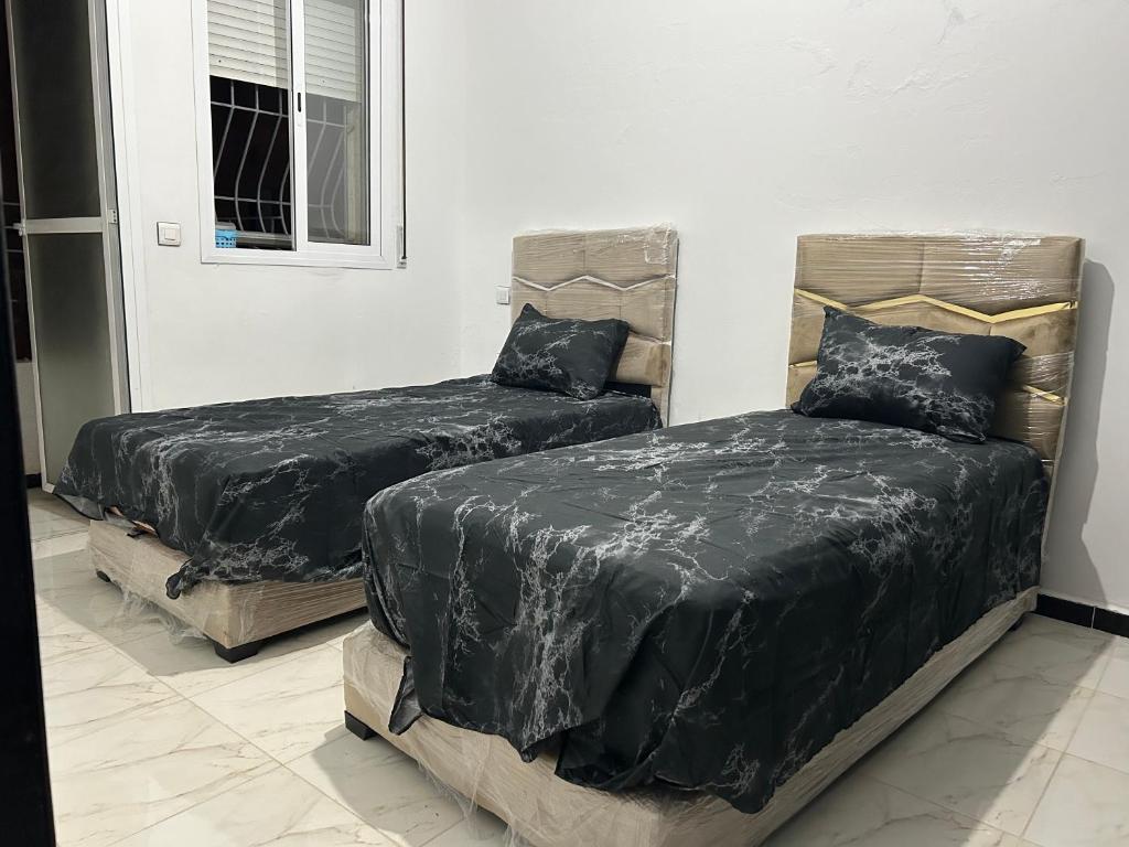 two beds with black covers in a room at شقة مفروشة قرب قاعة الحفلآت آحلام in Ksar el Kebir