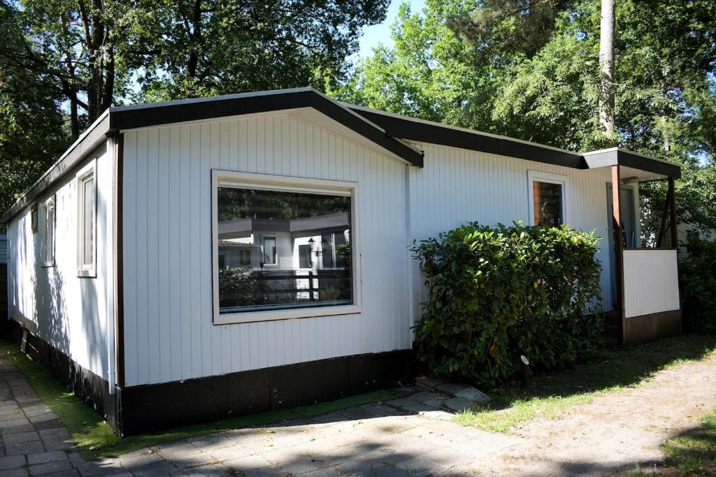 a small white building with a large window at Ruim en sfeervol chalet aan de rand van het bos in IJhorst
