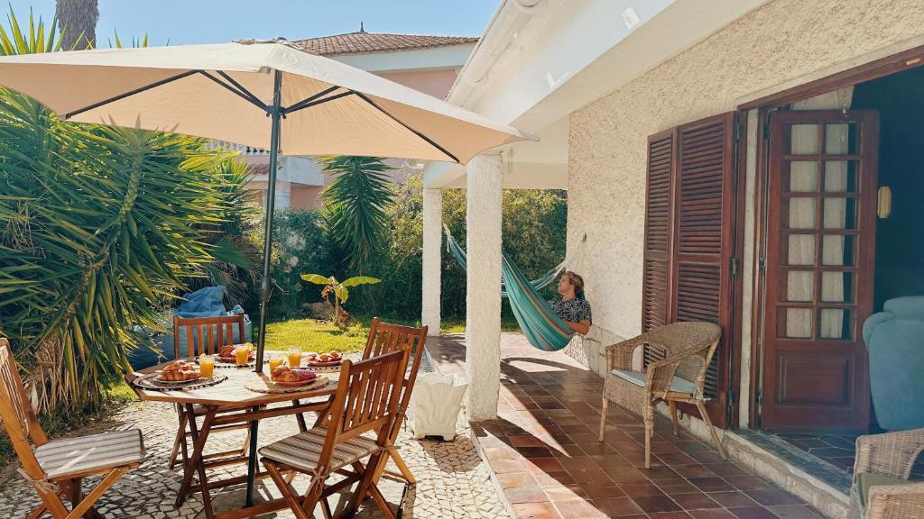 a woman sitting in a hammock under an umbrella on a patio at Coastal Garden Paradise Retreat- 6 min from the beach in Charneca