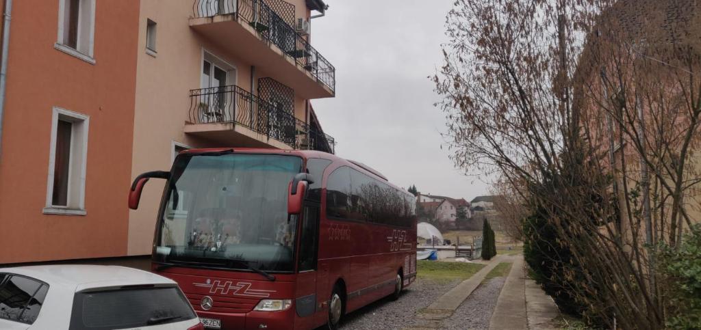 un bus rouge est garé à côté d'un bâtiment dans l'établissement Free Parking Pension, à Oradea