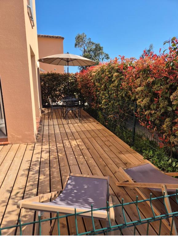 une terrasse en bois avec une table et un parasol dans l'établissement Les hameaux de Saint Cyprien - appartement avec jardin et piscine, à Lecci