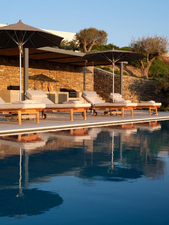 a pool with benches and umbrellas next to some water at Olithos Villas in Krotiri