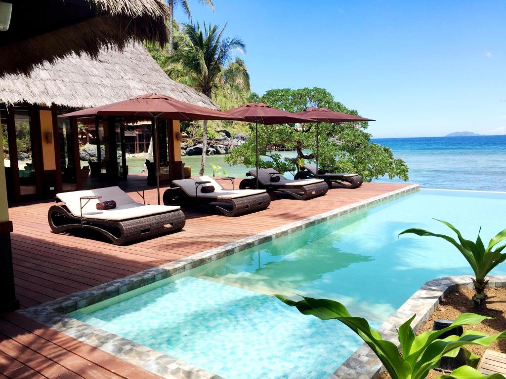 uma piscina com espreguiçadeiras e guarda-sóis junto ao oceano em Cauayan Island Resort and Spa em El Nido