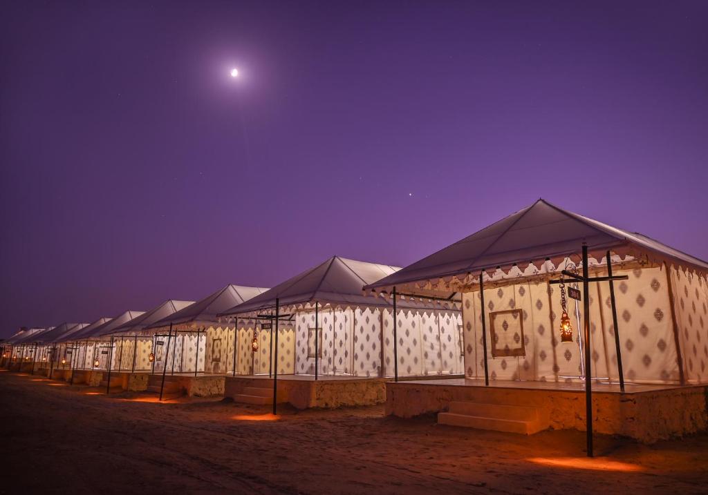 a row of tents at night with the moon in the sky at The Carvaans Resort-Luxury Desert Camp Jaisalmer in Sām