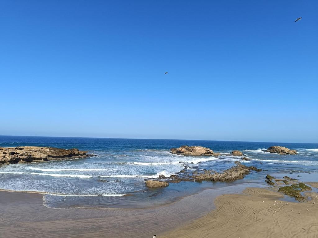 a beach with rocks and the ocean on a sunny day at Riad d'exception vue mer au coeur de la médina Essaouira - Mandji Dream in Essaouira