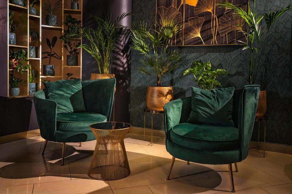a room with two green chairs and potted plants at Hotel Wellamarin in Zamárdi