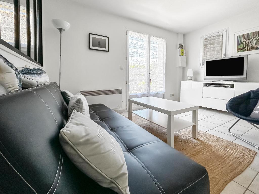 a living room with a black leather couch and a table at Maison cosy à deux pas du port et de la plage - Résidence port Guillaume in Dives-sur-Mer