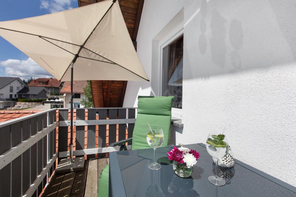 Una mesa de cristal con una sombrilla y flores en un balcón. en Haus Freudig - Tannenblick, en Höchenschwand