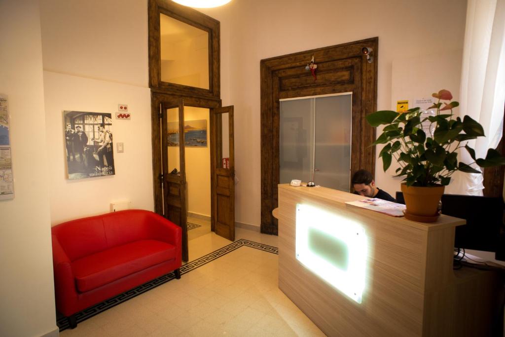 Ein Mann, der an einer Theke in einem Zimmer mit einem roten Stuhl sitzt. in der Unterkunft Napoli Milionaria B&B in Neapel