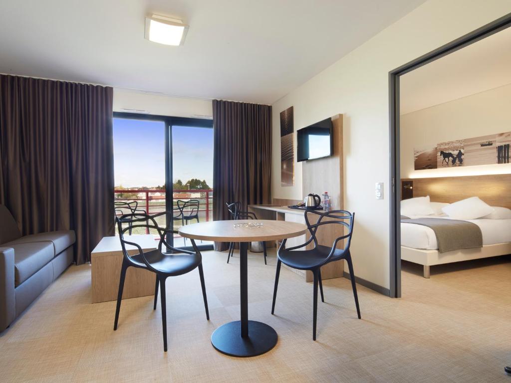 a hotel room with a table and chairs and a bed at Kyriad Prestige Residence & Spa Cabourg-Dives-sur-Mer in Dives-sur-Mer