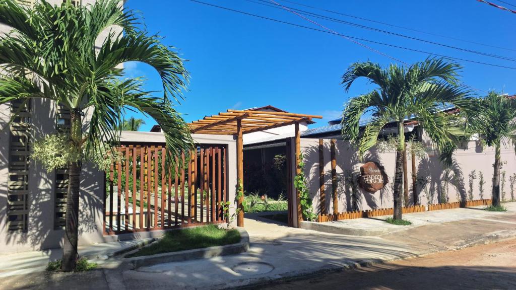 a fence with palm trees in front of a house at Pousada Maresia in São Miguel dos Milagres