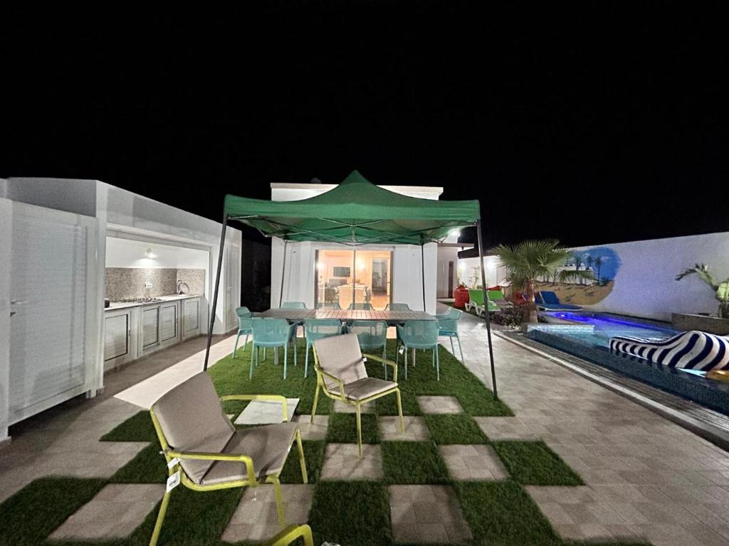 a patio with a table and chairs and a green umbrella at Villa SUN SQUARE DJERBA in Awlād ‘Umar