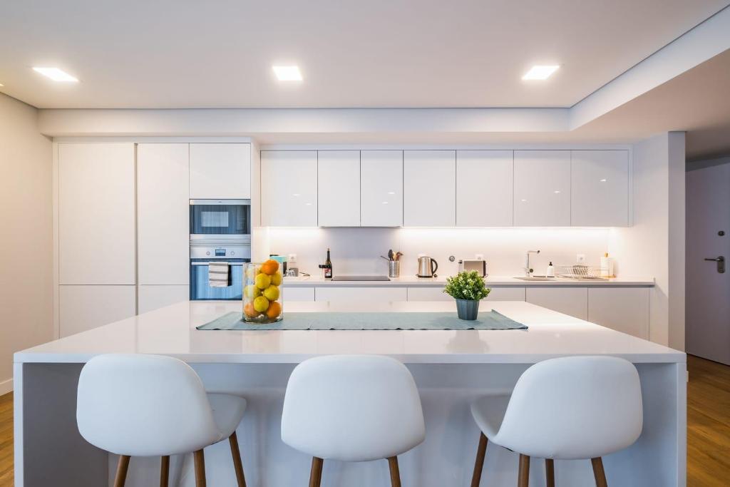 a kitchen with white cabinets and a large island with white chairs at The Shoreline 2 in Parede