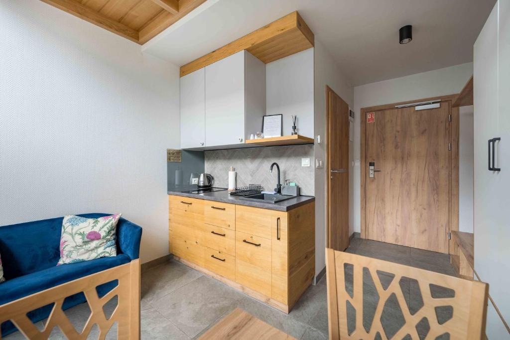 Small kitchenette beside blue sofa and wooden dining chair, apartment entry door visible.