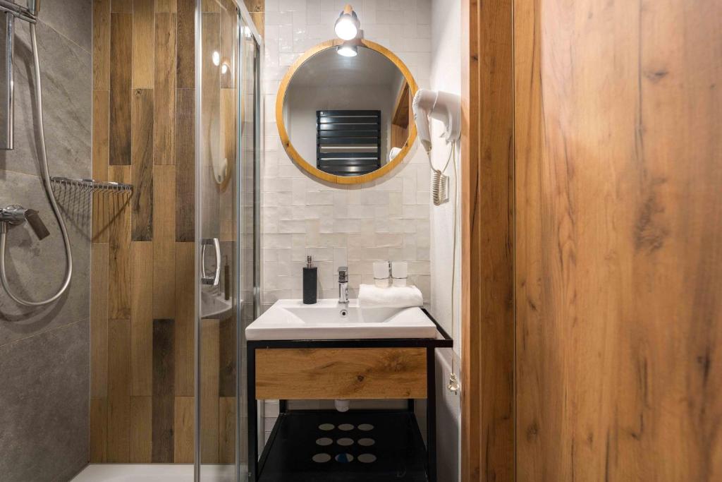 Compact bathroom featuring round mirror above sink, glass shower enclosure and wood-accent wall with hairdryer