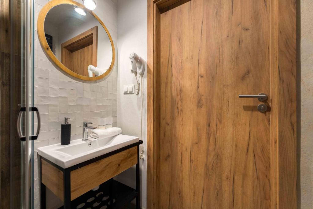 Compact bathroom with rectangular sink, round wooden-framed mirror, wall-mounted hairdryer, and wooden door.