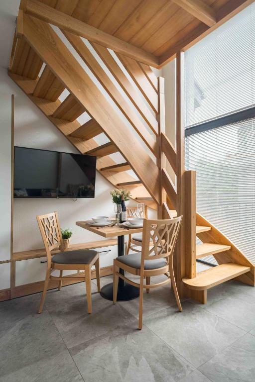 Compact living area with wooden staircase, small dining table and wall-mounted television by window.
