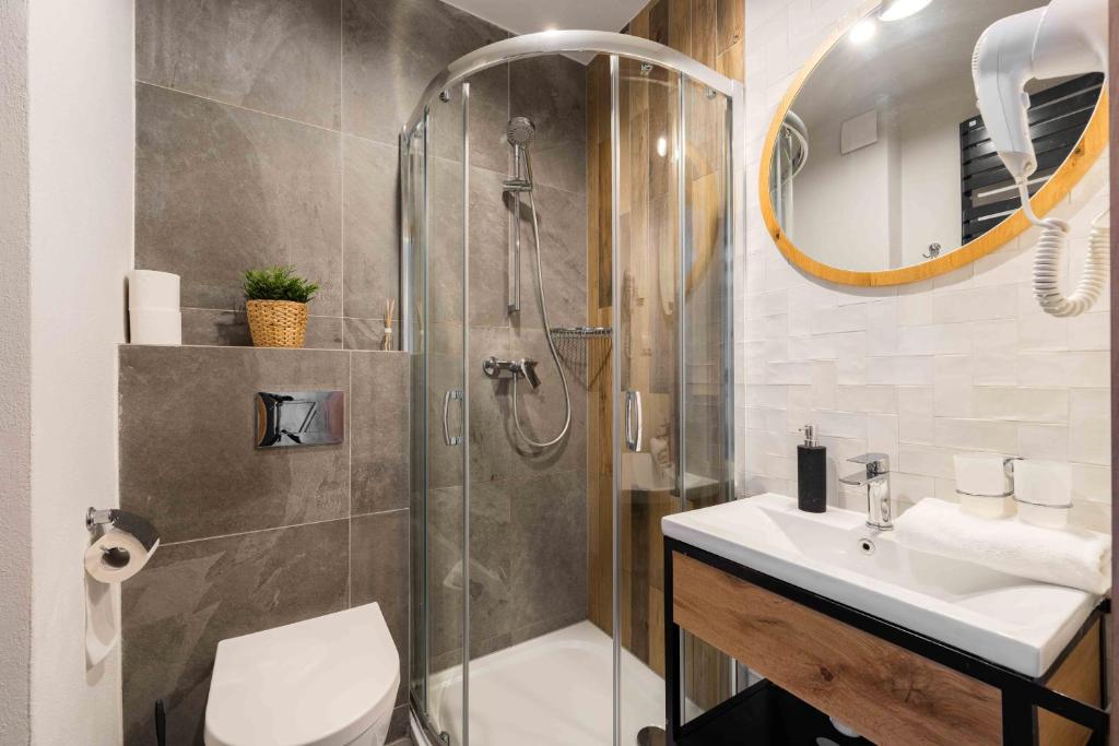 Modern bathroom with curved glass shower, wall-mounted toilet, sink and round mirror with neutral tiles