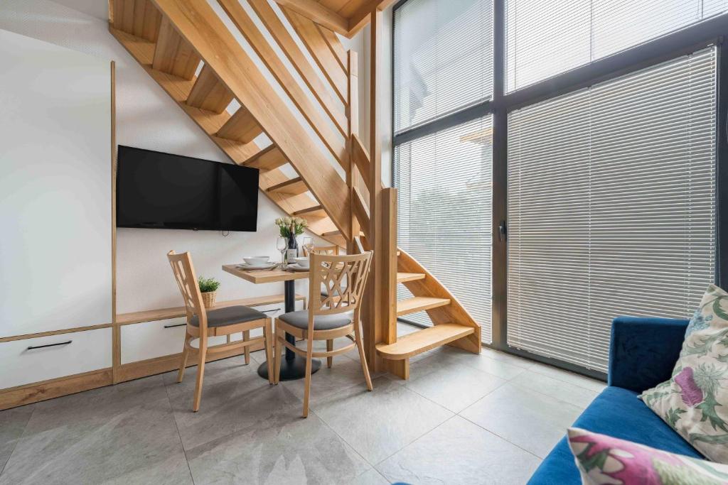 Small living area with wooden staircase, dining table for two, wall-mounted TV and large window blinds