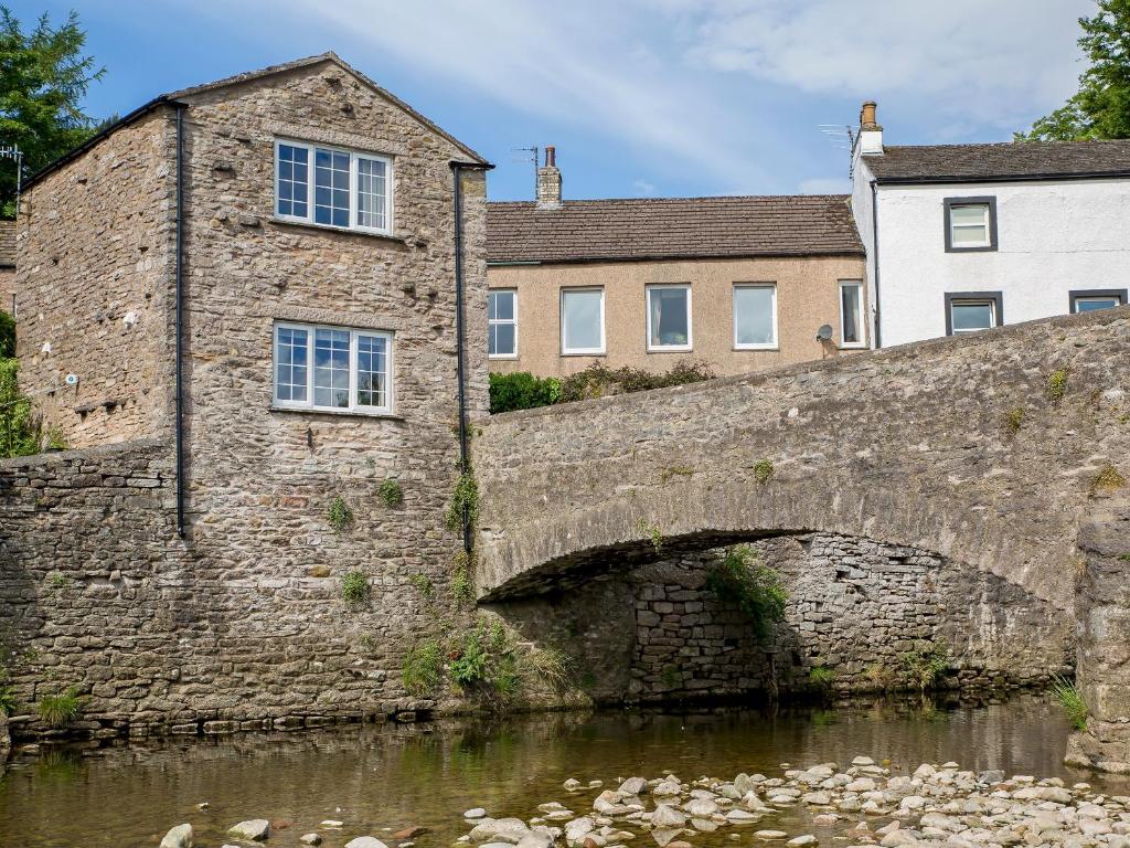 uma velha ponte de pedra sobre um rio com um edifício em Riverbank Cottage em Kirkby Stephen