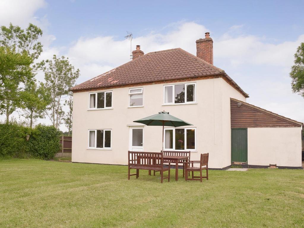 une maison blanche avec une table, des chaises et un parasol dans l'établissement Rose Farm Cottage, à Frostenden