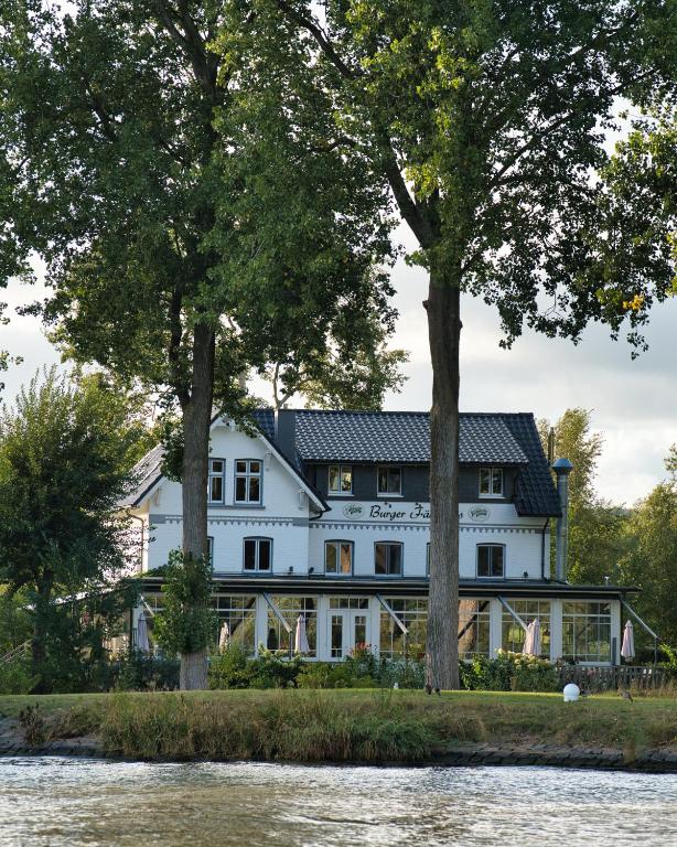 a large white house with trees next to a river at Burger Fährhaus in Burgerfeld