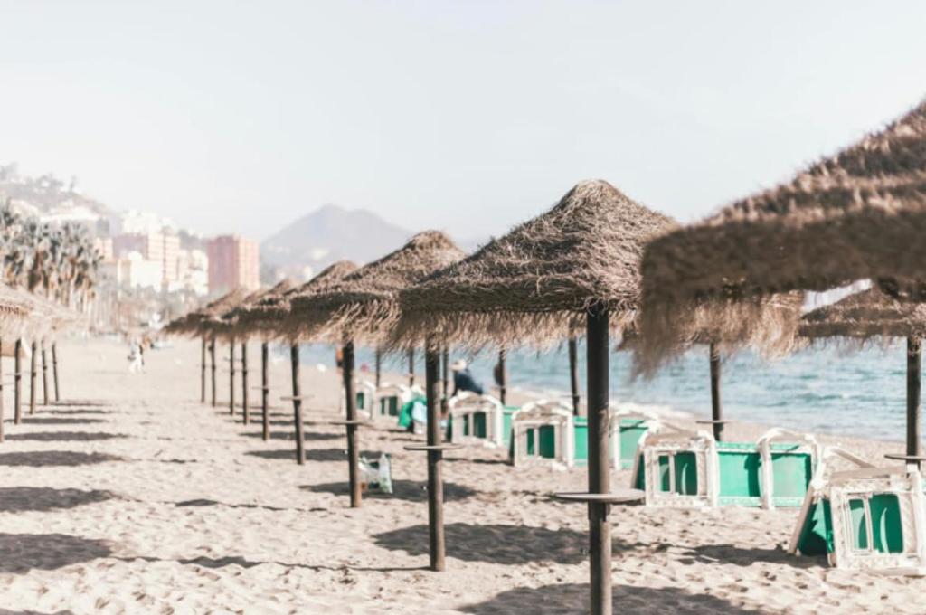 a row of straw umbrellas on a beach at Functional and Compact Studio in the Historic Center in Málaga