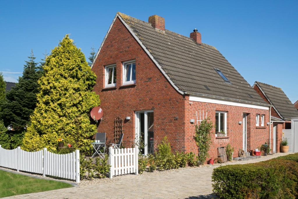 a red brick house with a white fence at Ferienhaus In Schwittersum Mit Großem Garten Und Panoramablick in Dornum