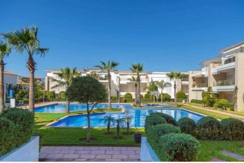 a swimming pool with palm trees and a building at Les perles de tamaris dar bouazza in Dar Mohammed Ould Haj Jilali