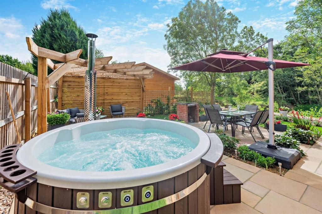a hot tub in a garden with a table and an umbrella at Woodlands Lavender Lake House in Long Bennington